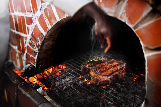 t-bone stake with rosemary grilling on chacoal cooking on a fire to make barbecue cusine in old style turnel at fire cooking kitchen