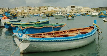 Fototapeta na wymiar Colorful authentic empty boats float on water in Marsaxlokk town on summer day. Maltese fishing village standing on sea bay. Famous and picturesque touristic landmark of Malta.
