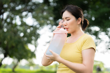 Asian woman taking a break to drink water after jogging at the park. The concept of drinking a lot of water for health. outdoor exercise