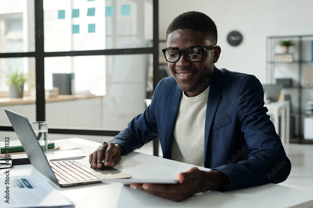 Poster young cheerful analyst or broker in eyeglasses and formalwear looking through online financial data 