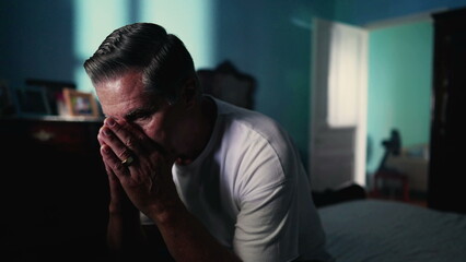 Pensive senior man stuggling with mental illness in bedroom. Desperate Lonely person suffering from anxiety and despair