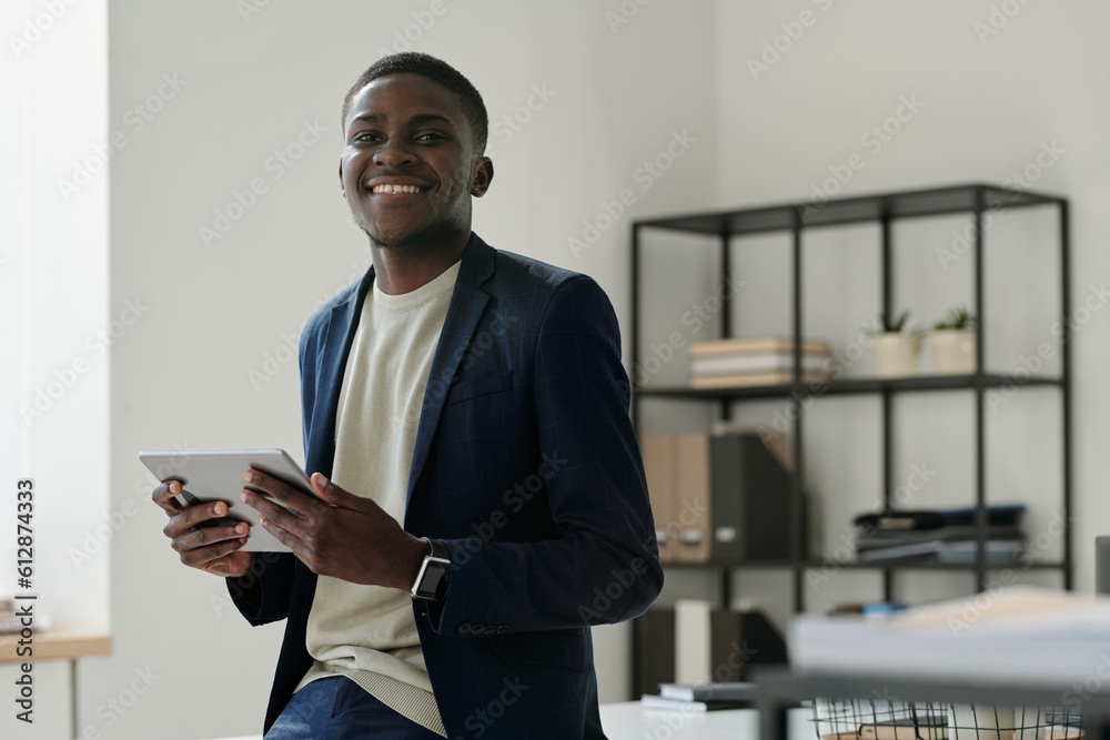 Aufkleber Young cheerful manager in formalwear looking at camera with smile while standing by workplace in openspace office and using tablet
