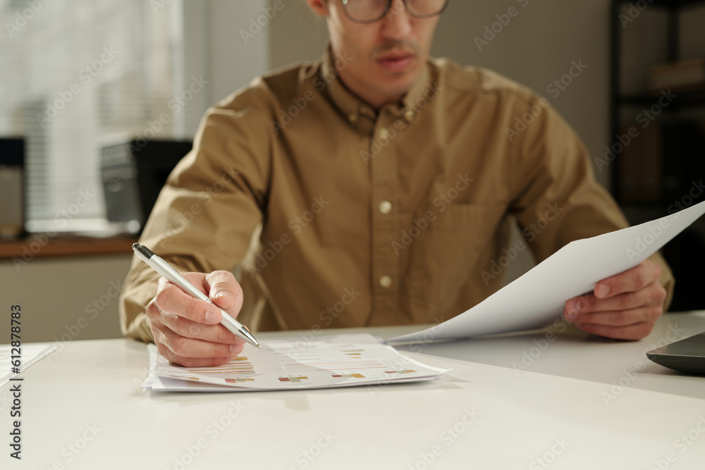 Poster focus on hand of male analyst or economist with pen over financial document with graphic data readin