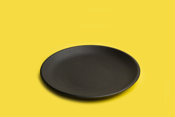 Un plato negro redondo sobre un fondo amarillo liso y aislado. Vista superior y de cerca. Copy space