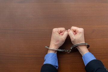 Top view, handcuffed hands of an arrested criminal on the table of the police station. copy space