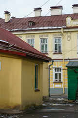 A one-story yellow building on the background of a historic house with a red roof. Old town with low houses and narrow streets. The historical center of a fashionable European city, tourist sites