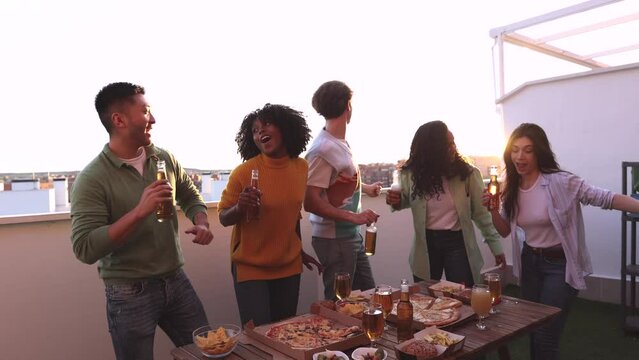 group of multiracial young friends gathering at a rooftop party drinking alcohol and dancing