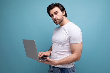 busy bearded brunette man in white tank top freelancer with laptop on studio background with copyspace