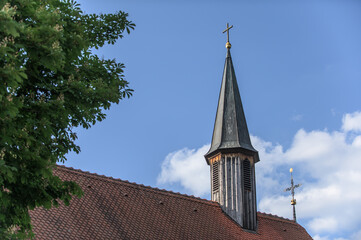 Hölzerner Kirchturm mit Spitzdach vor blauem Himmel mit Wolke