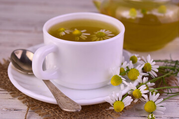 Obraz na płótnie Canvas Medicinal chamomile tea in a cup on a white wooden background. 