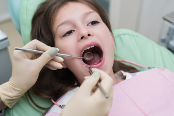The hands of a pediatric dentist carry out the examination procedure of a smiling cute little girl sitting on a chair in the hospital. Dentist's office. A little girl is sitting in the dentist's