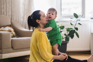 Sweet little boy hugging loving mother sitting on floor in living room at home happy woman enjoying...