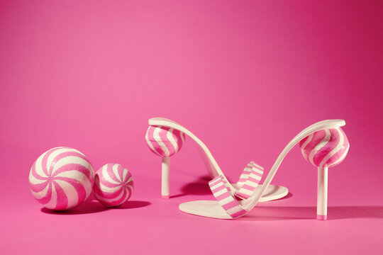 Sweet and unique high heels with candy lollipops, sweet charming style. Girl party time, summer vibes, cute fashion. Pink and white conceptual shoes. Pink background.
