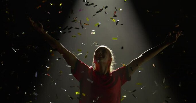 Female soccer football player spreading her hands against bright light and falling confetti. Super slow motion, shot on RED cinema camera