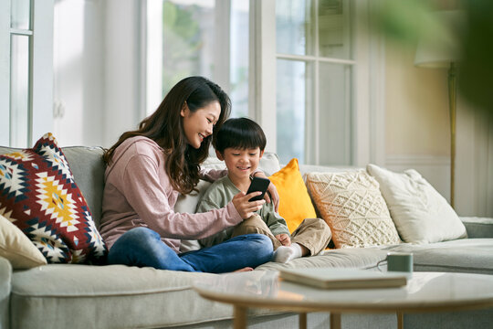 young asian mother sharing cellphone pictures with son at home