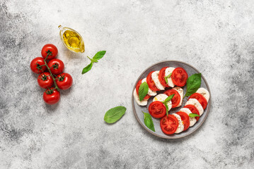 Caprese salad. Italian salad with chopped tomatoes, mozzarella, basil, olive oil on a gray background. Top view, flat lay