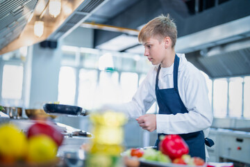 Young chef cooking at restaurant kitchen.