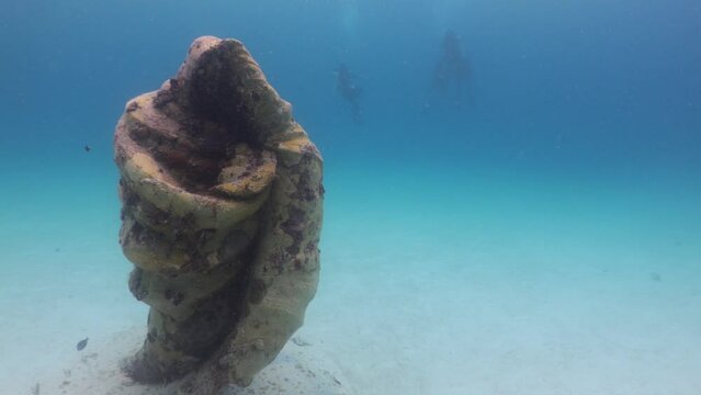 Estatua bajo el mar con forma de concha y silueta de virgen y buzos al fondo explorando en arrecife del caribe mexicano.