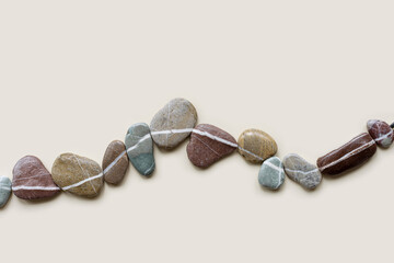 Fototapeta premium Creative arrangement of natural colored stones. Smooth pebbles in row on beige background. Minimal trend summer flat lay, top view still life composition with sea pebble on the same line