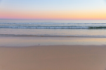Waves of the sea from the beach at sunset, with shades of color in the sky