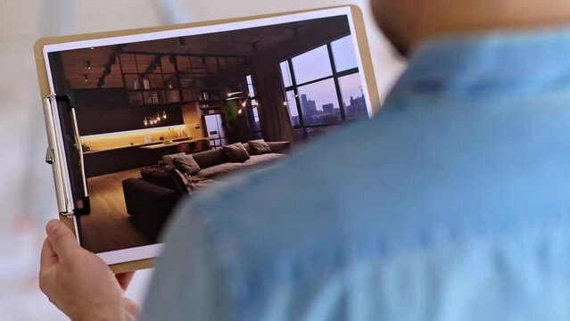 close up Home owner looks at picture with interior design in loft style against ladder near wall man in glasses imagining apartment after renovation process