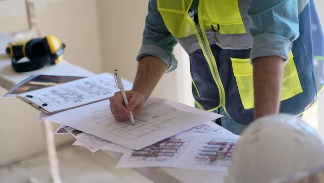 Engineer in vest studying project documentation getting ready for apartment reconstruction man reading papers near protective hardhat construction safety equipment