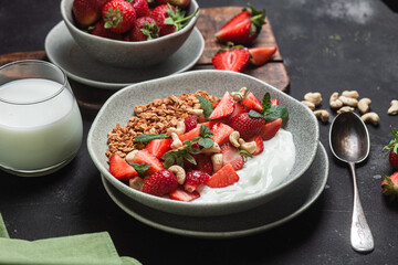 Granola with yogurt and strawberries in a plate on a dark background