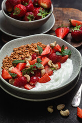 Granola with yogurt and strawberries in a plate on a dark background