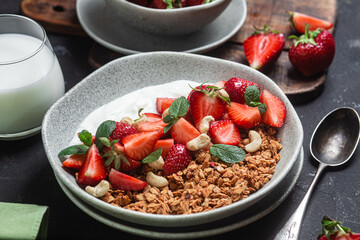 Granola with yogurt and strawberries in a plate on a dark background