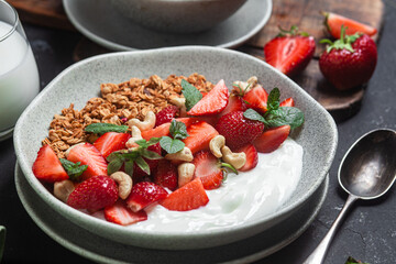 Granola with yogurt and strawberries in a plate on a dark background