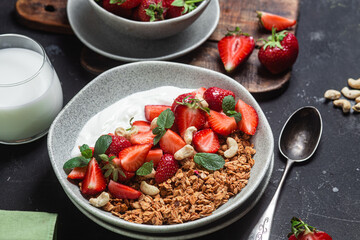 Granola with yogurt and strawberries in a plate on a dark background