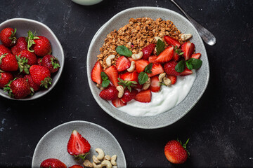 Granola with yogurt and strawberries in a plate on a dark background