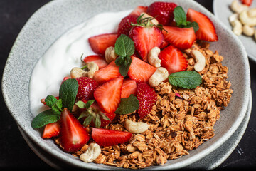 Granola with yogurt and strawberries in a plate on a dark background