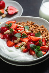 Granola with yogurt and strawberries in a plate on a dark background