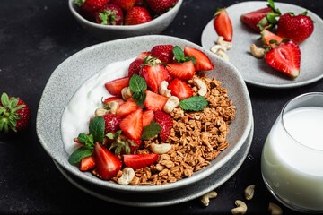 Granola with yogurt and strawberries in a plate on a dark background