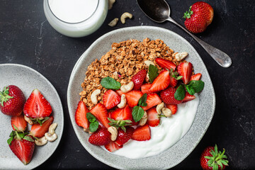 Granola with yogurt and strawberries in a plate on a dark background