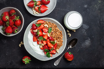 Granola with yogurt and strawberries in a plate on a dark background