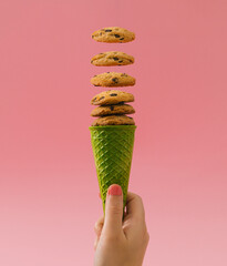 Trendy green waffle ice cream cone with chocolate cookies on bright pink background. Minimal food...