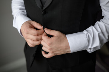 Obraz premium Portrait of a fashionable man fastening a button on jacket, close-up.Wedding day. Young modern businessman.