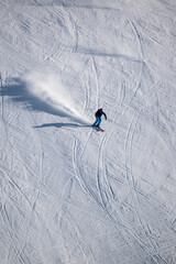 Skiing down mountain slope with white snow powder projecting from behind skier wearing black and...