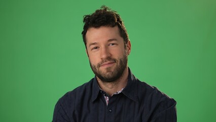 Fototapeta premium Handsome dreamful bearded young guy 20s in hoodie isolated on green screen chroma key background in studio. People sincere emotions, lifestyle concept. Smiling looking at the camera.