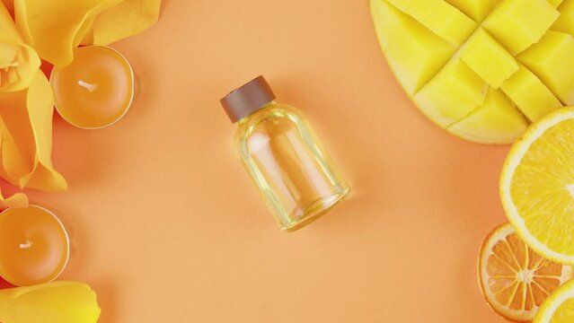 Jar of cosmetic oil perfume on the table . Composition of citrus slices, flowers, mango, aroma candles on orange background close-up, top view, zoom. Summer bright texture studio shot.