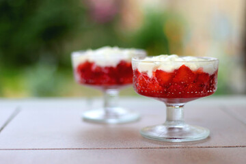 Two bowls of strawberries and whipped cream, served in a garden. Selective focus.