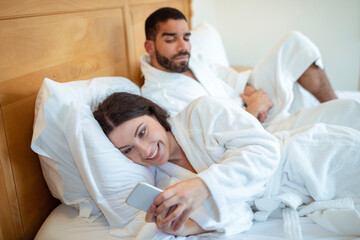 Fototapeta premium Suspicious husband seeing wife messaging on smartphone at home