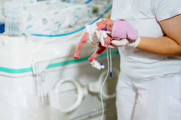 Doctor in ICU examining premature born child. Female nurse with premature born baby in intensive care unit holding infant in her hands.