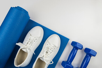 Fitness accessories concept. Photo of dumbbells and white sneakers on a sports mat