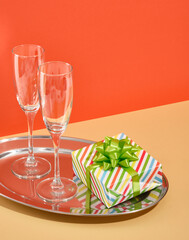 Champagne and wine glasses on shiny metal tray. Holiday gift with green bow. Place for text. Romantic atmosphere.