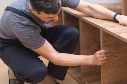 Custom furniture production and fixing man in coveralls installing shelves on wooden rack for home office interior specialist working with quality wood materials