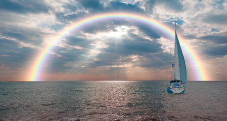 Yacht sailing in open sea at stormy day with rainbow - Anchored sailing yacht on calm sea with tropical stor