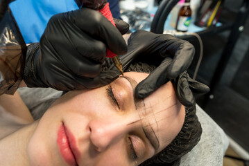 The cosmetologist makes a permanent makeup of the eyebrows